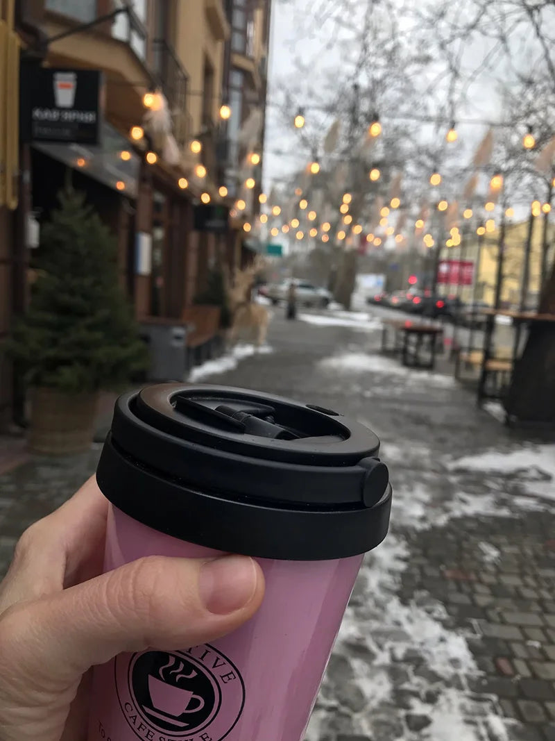 Hand holding a pink travel mug on a city street