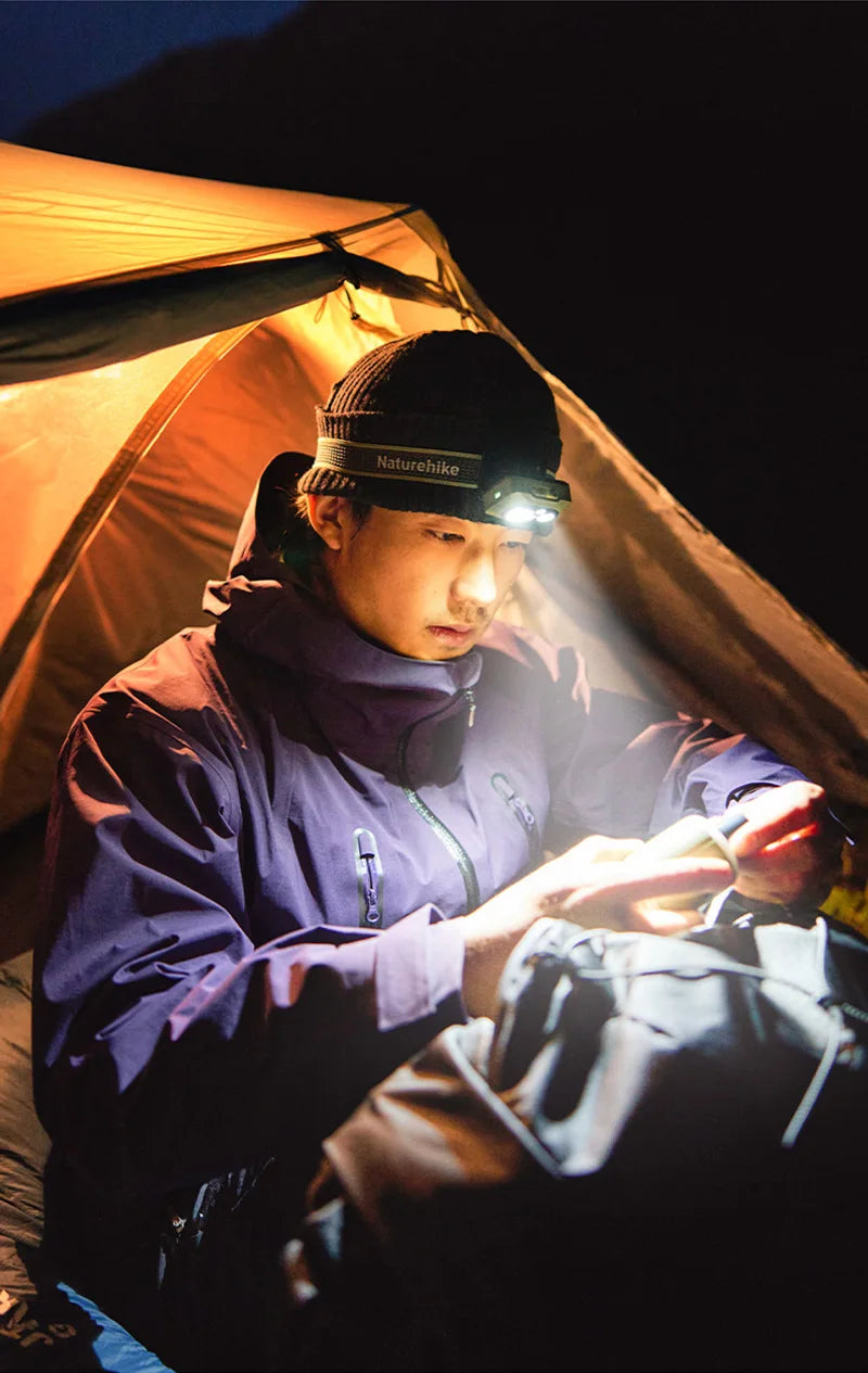 Camper looking through gear by headlamp light in a tent doorway