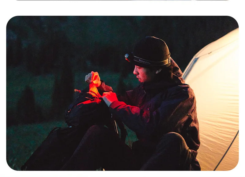 Person using the headlamp's red light beside a tent at night