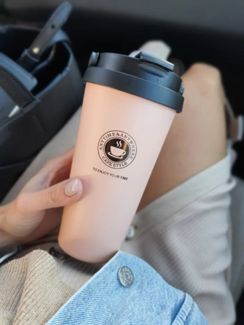Hand holding a pink travel mug in a car