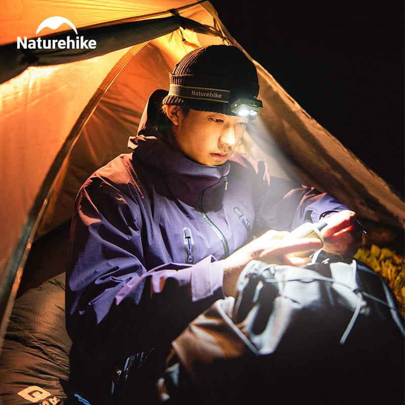 Person reading by headlamp light in a tent doorway