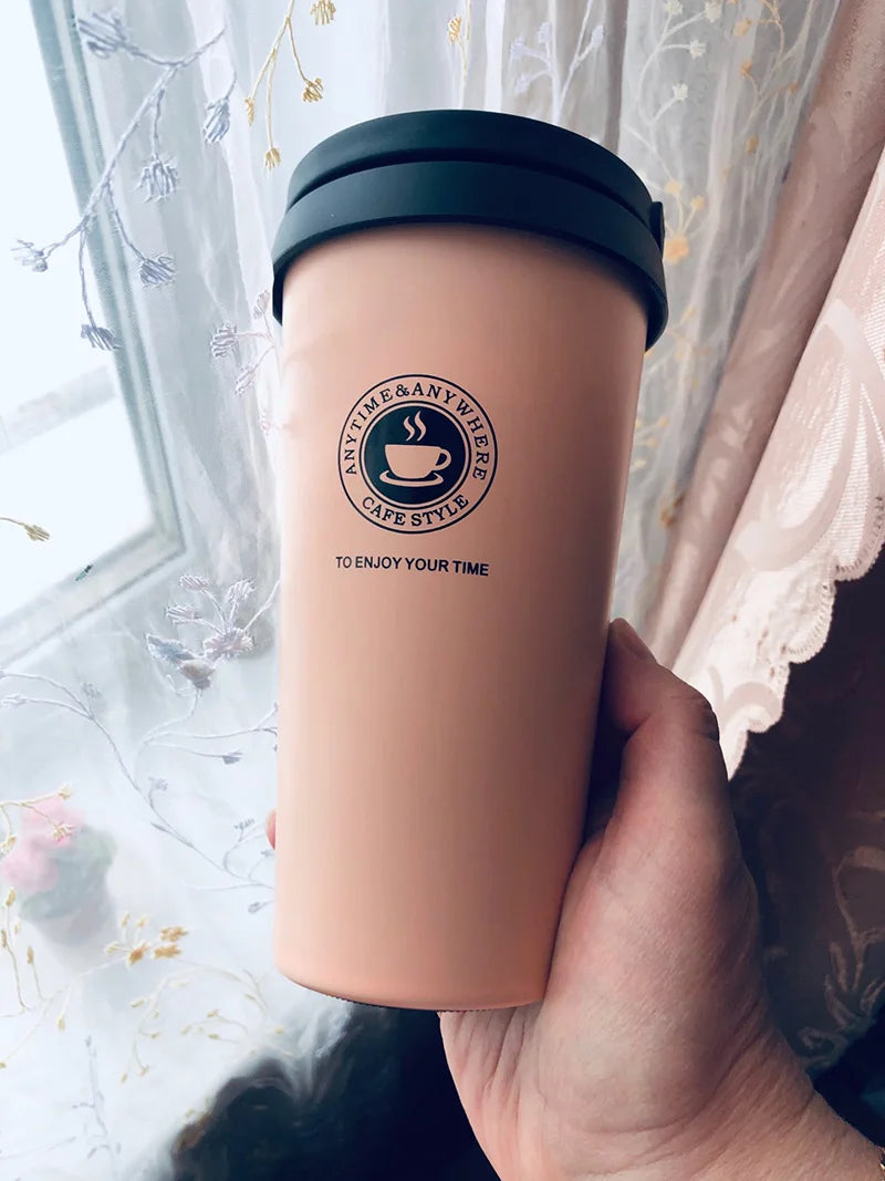 Hand holding a pink travel mug by a window