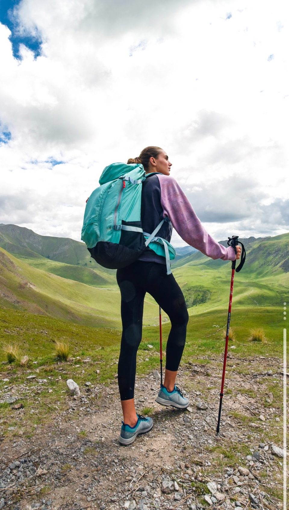 Hiker leaning on trekking poles on a grassy mountain trail